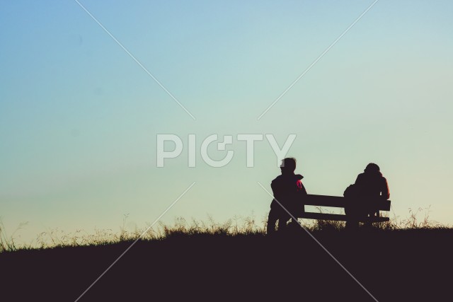 夕暮れの丘に座る人々のシルエット