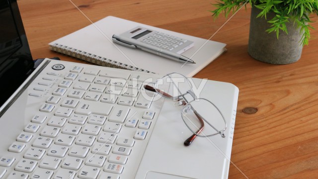 木製デスクのパソコンと眼鏡で表すデスクワーク