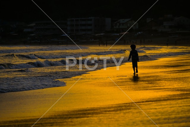 夕暮れの波打ち際で遊ぶ子供