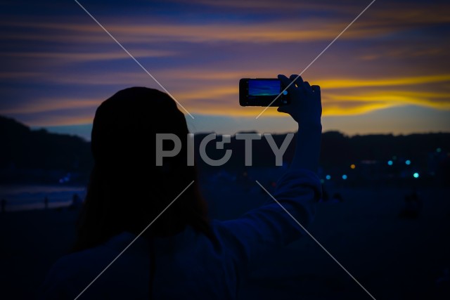 スマホで夕暮れを撮る女性